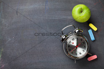 Colorful chalk, alarm clock and apple on blackboard background