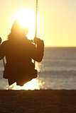 Woman silhouette swinging at sunset on the beach