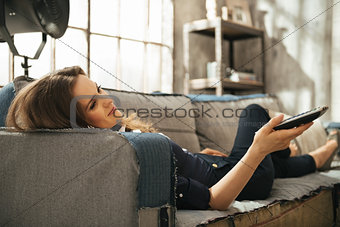 Relaxed woman lying on sofa and watching tv in loft apartment