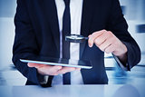 Composite image of businessman looking at his tablet through magnifying glass