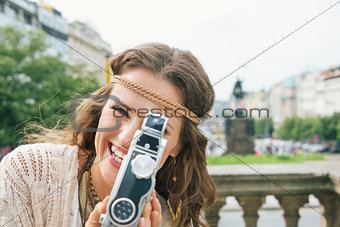Joyful hippy-looking woman tourist using retro camera in Prague