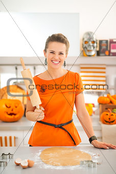Smiling halloween dressed woman with rolling pin in kitchen