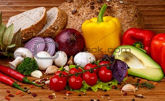 Fresh vegetables and spices: tomatoes, peppers, mushrooms, herbs, bread, avocado on wooden background