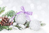 Christmas baubles and purple ribbon over snow bokeh background