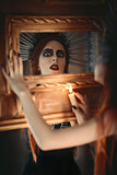 Strange goth girl holding candle in hand and looking into mirror