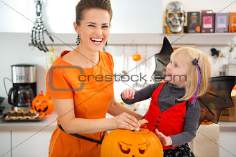 Girl in bat costume with mother preparing Jack-O-Lantern