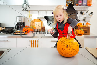 Halloween dressed girl creating pumpkin Jack-O-Lantern