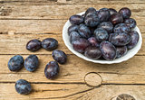 Plate full of fresh plums on a wooden background