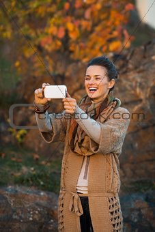 Woman taking photo with cell phone in autumn outdoors in evening
