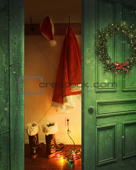 Open rustic door with Santa outfit hanging on hooks