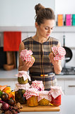 Woman in kitchen holding preserves and looking at jars