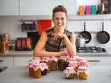 Happy, proud woman in kitchen with jars of home-preserved fruits