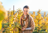 Smiling young woman winegrower standing in autumn grape field