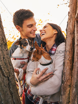 Happy young couple holding dogs in park and smiling