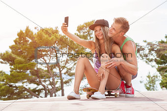 Happy couple with sitting on skateboard and taking a selfie 