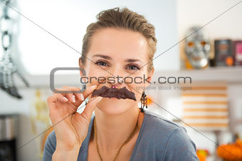 Funny modern housewife making mustache with Halloween biscuit
