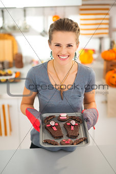 Smiling woman holding tray with homemade Halloween biscuits