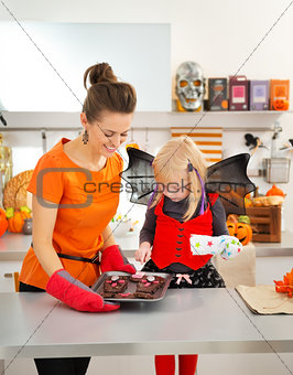 Halloween dressed girl with mother holding tray with biscuits