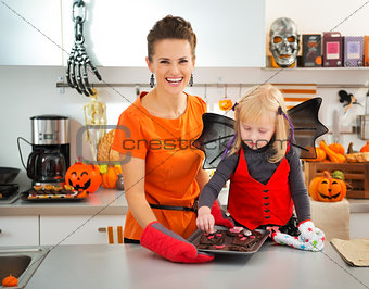 Girl with mother holding tray with Halloween biscuits in kitchen
