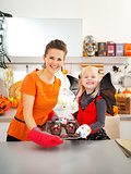 Girl with mother holding tray with Halloween cookies in kitchen
