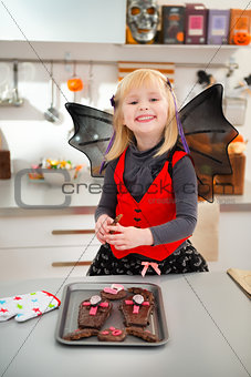 Funny girl in bat costume holding freshly Halloween cookies