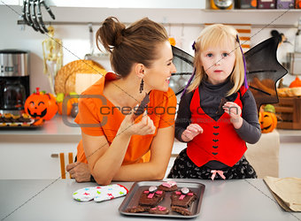 Girl in bat costume with smiling mother eating Halloween cookies