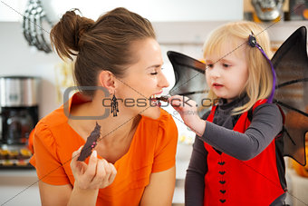 Girl in bat costume with mother eating Halloween biscuits