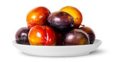 In front mix of red and violet plums on white plate
