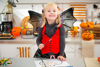 Girl in halloween bat costume drawing Jack-O-Lantern on paper