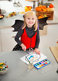 Halloween dressed girl drawing pumpkin Jack-O-Lantern on paper