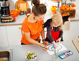 Halloween dressed girl with mother drawing Jack-O-Lantern