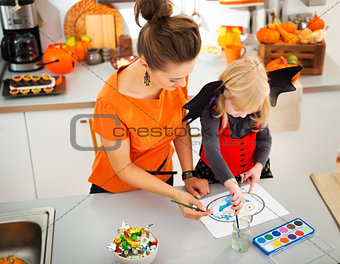 Halloween dressed girl with mother drawing Jack-O-Lantern