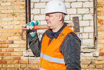 Construction worker with sledgehammer near the brick wall