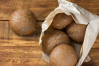 Rye bread in paper bag on wooden background.