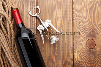 Red wine bottle and corkscrew on wooden table