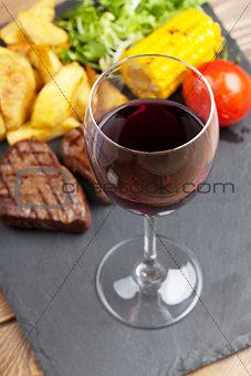 Red wine glass and steak with grilled potato, corn, salad