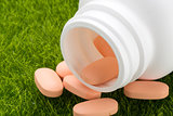 Close up pill bottle spilling orange pills on to grass