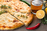 Top view of calzone pizza or chicken mushroom pie with pepper, lemon, rosemary and tea on linen fabric background