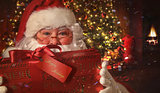Closeup of Santa holding gift with Christmas scene in background