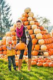 Beautiful woman with little girl holding pumpkins on farm