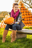 Portrait of woman sitting on the bench with pumpkin on farm
