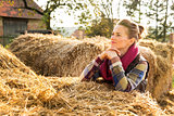 Portrait of young woman staying next to stack of hay on farm