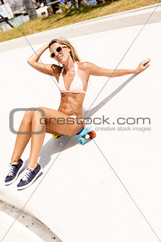 sexy suntanned lady sitting on the blue penny board in the park