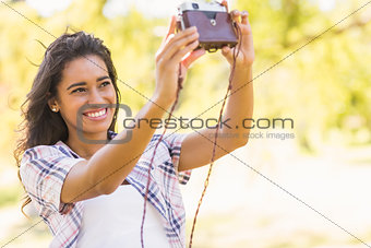 Pretty brunette taking a selfie with retro camera in the park