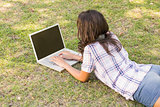 Pretty brunette lying in the grass and using laptop