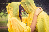 Cute couple wearing protection cape and hugging under the rain