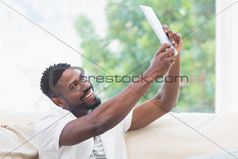 Man using his tablet on couch to take selfie