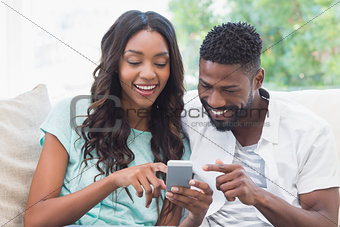 Happy couple on the couch using phone