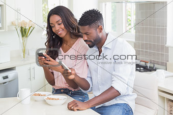 Happy couple using their phones at breakfast