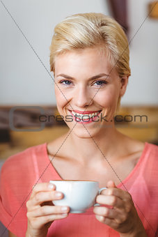 Pretty blonde woman smiling at camera and holding a cup of coffee